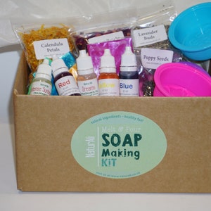 May include: A brown cardboard box with a green and white sticker that says "NaturAli Melt & Pour SOAP Making KIT". The box contains a variety of ingredients for making soap, including dried flowers, essential oils, and molds.