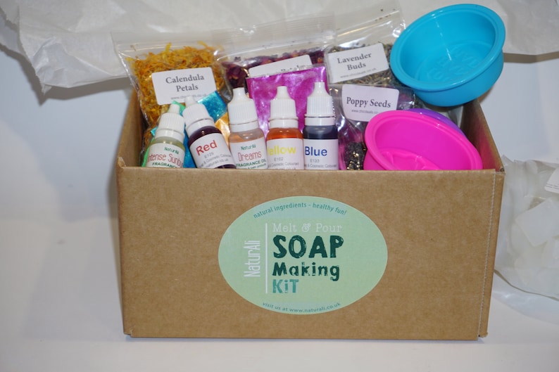 May include: A brown cardboard box with a green and white sticker that says "NaturAli Melt & Pour SOAP Making KIT". The box contains a variety of ingredients for making soap, including dried flowers, essential oils, and molds.