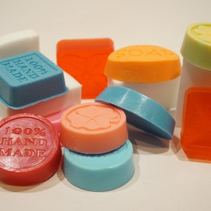 May include: Assortment of colorful handmade soap bars with various scents and designs. Some bars feature the text "100% HAND MADE".