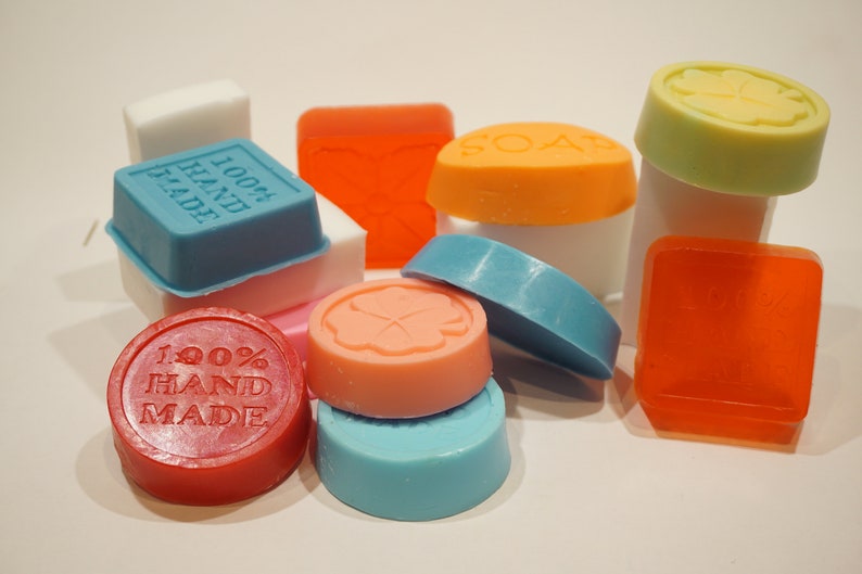 May include: Assortment of colorful handmade soap bars with various scents and designs. Some bars feature the text "100% HAND MADE".