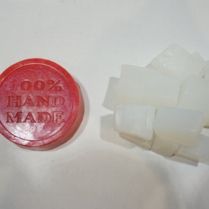 May include: A red round soap base with the text "100% HAND MADE" printed on it. Next to the base are several white soap bars.