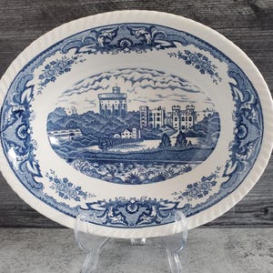 May include: Oval serving platter with a blue and white transferware design. The platter features a detailed landscape scene of a castle and surrounding buildings. The rim has a decorative floral and scroll pattern.