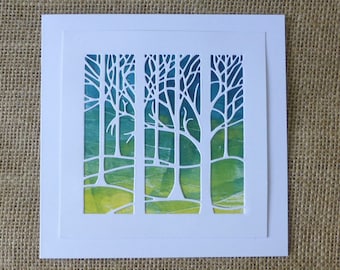 Può includere: Un biglietto bianco con un disegno ritagliato di tre alberi. Gli alberi sono in silhouette su uno sfondo acquerellato verde e blu.