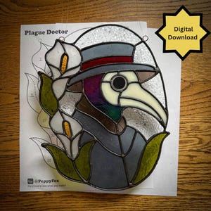 May include: A stained glass suncatcher depicting a plague doctor wearing a top hat, accompanied by white calla lilies with yellow centres. The piece features textured clear glass, dark grey, and green tones. Includes a pattern sheet labelled Plague Doctor.