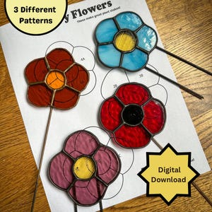 Op de afbeelding: Drie glas-in-lood bloemenontwerpen met metalen stelen. De bloemen zijn rood, blauw en roze. De ontwerpen zijn genummerd en met letters gemarkeerd. De tekst "3 Different Patterns" en "Flowers" staat bovenaan de pagina. De tekst "These make great plant stakes!" staat onder de titel. De tekst "Digital Download" staat in een gele stervorm onderaan de pagina.