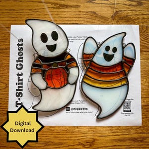 Può includere: Due ornamenti a forma di fantasma in vetro colorato con facce sorridenti. Un fantasma indossa una camicia di zucca arancione e marrone, l'altro una camicia a righe. Le parole "T-Shirt Ghosts" e "Digital Download" sono visibili.