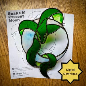 May include: A stained glass snake and crescent moon design in shades of green, white, and blue. The artwork is on a white paper with the text "Snake & Cresent Moon". A digital download icon is in the lower right corner.