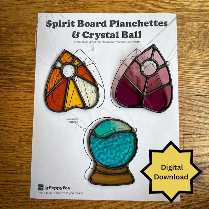May include: Three colorful spirit board car charms. The charms include two planchette designs in orange, yellow, and red, and pink and purple. The third charm is a crystal ball design with turquoise and green colors. The text "Spirit Board Planchettes & Crystal Ball" is at the top.