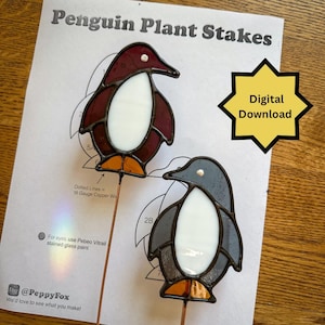 May include: Two stained glass penguin plant stakes with white bellies and orange feet, one with dark red wings and one with dark grey wings. They are displayed on a printed pattern sheet titled Penguin Plant Stakes with Digital Download text.