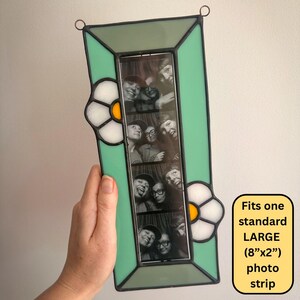 May include: A rectangular stained glass photo frame with a mint green border and two white flower accents featuring yellow centers. The frame holds a vertical black and white photo strip. Text on the image states: Fits one standard LARGE (8"x2") photo strip.