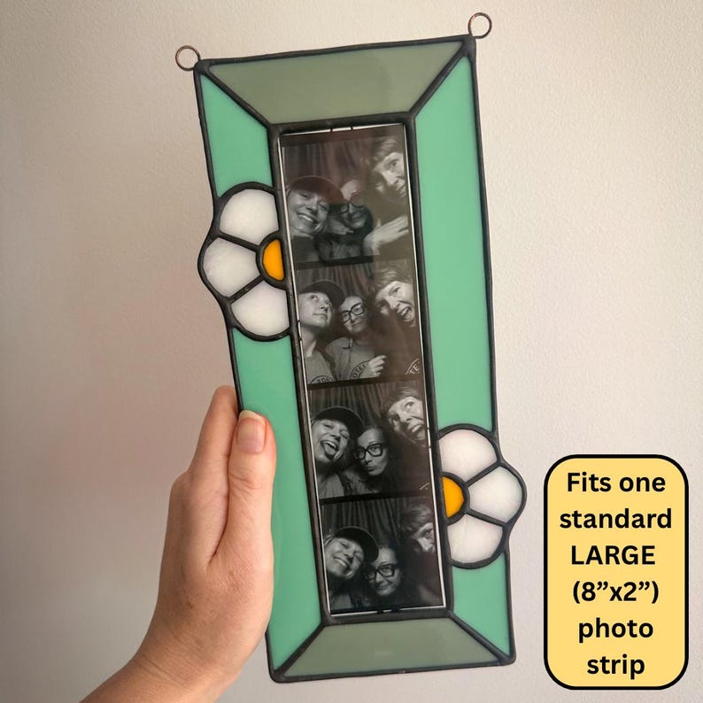 May include: A rectangular stained glass photo frame with a mint green border and two white flower accents featuring yellow centers. The frame holds a vertical black and white photo strip. Text on the image states: Fits one standard LARGE (8"x2") photo strip.