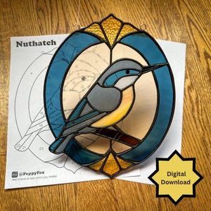 May include: Stained glass Nuthatch bird suncatcher with blue, yellow, and gray hues. The bird is perched on a branch within a blue oval frame. A paper with the word "Nuthatch" and a "Digital Download" starburst are also visible.