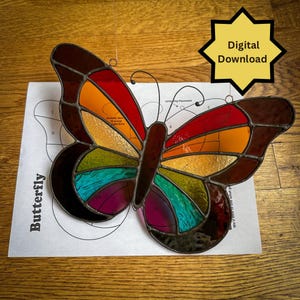 May include: A stained glass butterfly with a pattern of red, orange, yellow, green, blue, and purple. The butterfly is on a white sheet of paper with a pattern for assembling a stained glass butterfly.