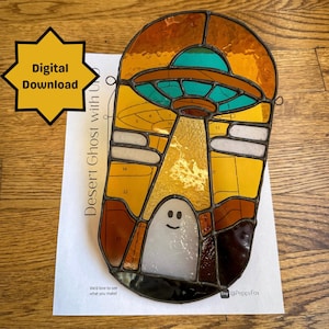 May include: A stained glass pattern of a ghost with a UFO above it. The pattern is numbered for a stained glass project. The text "Desert Ghost with UFO" is written on the paper.