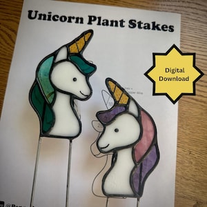 May include: Two stained glass unicorn plant stakes with metal rods. One features a white head, yellow horn, and green mane. The other has a white head, yellow horn, and purple and pink mane. The background paper reads Unicorn Plant Stakes and Digital Download.
