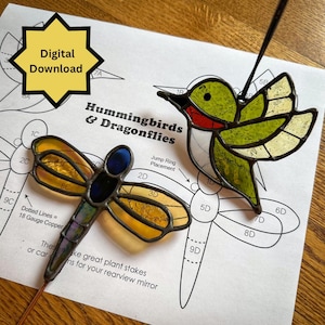 May include: Two stained glass ornaments: a dragonfly and a hummingbird. The dragonfly has yellow and blue wings, and the hummingbird is green, red, and yellow. The image also shows a paper with the words "Hummingbirds & Dragonflies" and "Digital Download".