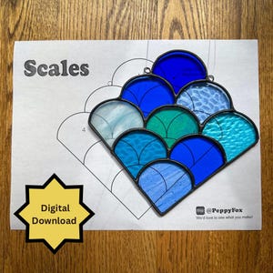 Puede incluir: Un vitral con un diseño de escamas, con tonos de azul, turquesa y vidrio transparente, con un marco de metal negro. La palabra "Scales" está impresa encima del diseño. Un gráfico de estrella amarilla dice "Digital Download".