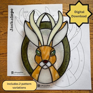 May include: A stained glass jackalope with a brown and white body, green eyes, and white antlers. The design is on a printed pattern sheet with the text "Jackalope" and "Digital Download". Includes 2 pattern variations.