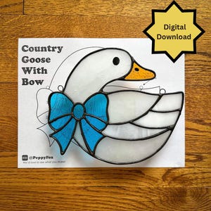 May include: A stained glass pattern featuring a white goose with a blue bow, a yellow beak, and black eyes. The text "Country Goose With Bow" is above the goose. A yellow starburst graphic reads "Digital Download".