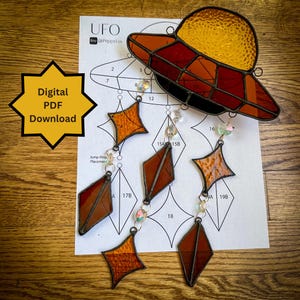 May include: A stained glass UFO mobile kit with a pattern for a flying saucer and five diamond-shaped stars. The kit includes instructions and a list of materials needed to create the mobile.