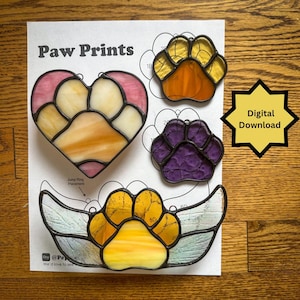 May include: Stained glass paw print designs in various colors, including yellow, orange, purple, and pink. The designs are on a white paper with the text "Paw Prints" and "Digital Download".