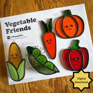 Könnte beinhalten: Ein Set aus fünf Buntglas-Gemüseornamenten, bestehend aus einem Maiskolben, einer Erbsenschote mit Kupferdraht, einer Karotte, einem Kürbis und einer roten Paprika. Jedes Teil hat ein lächelndes Gesicht und liegt auf einer Anleitung namens Vegetable Friends.