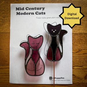 May include: Two stained glass cat plant stakes. One is black, the other is shades of pink. The stakes are on a sheet of paper with the text "Mid Century Modern Cats" and "Digital Download".