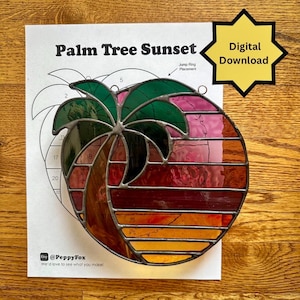 Puede incluir: Un vitral circular que representa un atardecer con palmeras, con tonos verdes, rosas, naranjas y rojos. La obra de arte está sobre un papel con el texto "Palm Tree Sunset" y "Digital Download". El fondo es de madera.