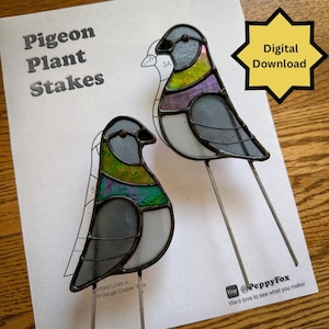 Op de afbeelding: Twee tiffany glazen duif plantenstekers met grijze, witte, groene en paarse glasstukjes en donkere soldeerlijnen. De stekers liggen op een geprint patroonblad met de tekst Pigeon Plant Stakes en een Digital Download ster-icoon.
