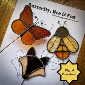 May include: Three stained glass plant stakes, a butterfly, a bee, and a fox. The butterfly is orange and brown, the bee is yellow and brown, and the fox is black and brown. The stakes are on a white background with a black and white outline of each animal. The text "Butterfly, Bee & Fox" and "These make great plant stakes!" is printed on the background. The text "Digital Download" is printed on a yellow star.
