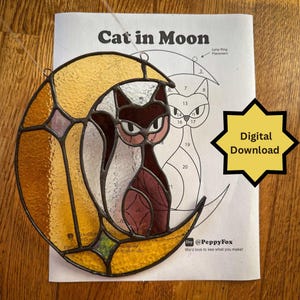 Puede incluir: Gato de vidriera en un diseño de media luna. El gato es de color rojo oscuro y blanco, sobre una luna amarilla y naranja. El patrón está en una hoja blanca con el texto "Cat in Moon".