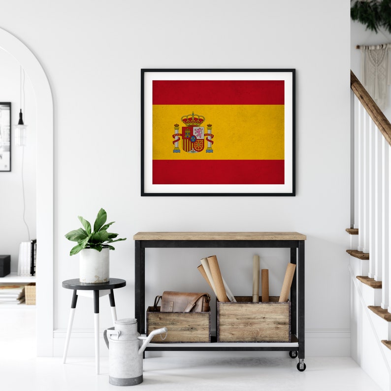May include: Framed print of the Spanish flag, featuring red and yellow horizontal stripes with the Spanish coat of arms. The artwork is displayed in a black frame, adding a touch of elegance to the wall decor. The image is in a bright, modern interior.