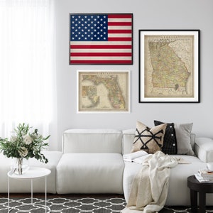 May include: A white sectional sofa with a beige throw blanket and two decorative pillows. The sofa is in front of a white wall with three framed prints: a vintage map of Florida, a vintage map of Georgia, and an American flag.