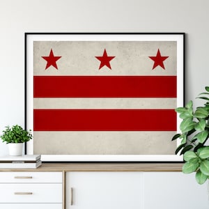 May include: A framed print of the flag of Washington, D.C. The flag is white with three horizontal red stripes and three red five-pointed stars.