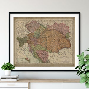 May include: A vintage map of Austria-Hungary, printed on aged paper with a brown, green, and red color scheme. The map is framed in a black frame and is displayed on a shelf with a book.