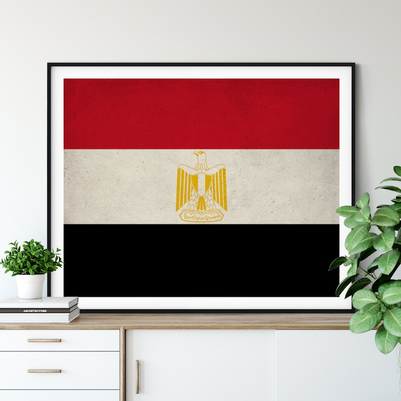 May include: A framed print of the flag of Egypt. The flag is red, white, and black with a gold eagle in the center.