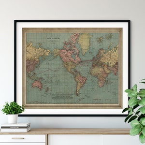 May include: Vintage world map print in a black frame. The map is in a Mercator projection and shows the continents in shades of green, yellow, and pink. The oceans are a light blue color. The map includes a title "The World" and a legend.