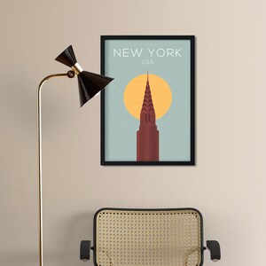 May include: A black framed poster with a minimalist illustration of the Chrysler Building in New York City, USA. The building is red and the background is blue with a yellow sun.
