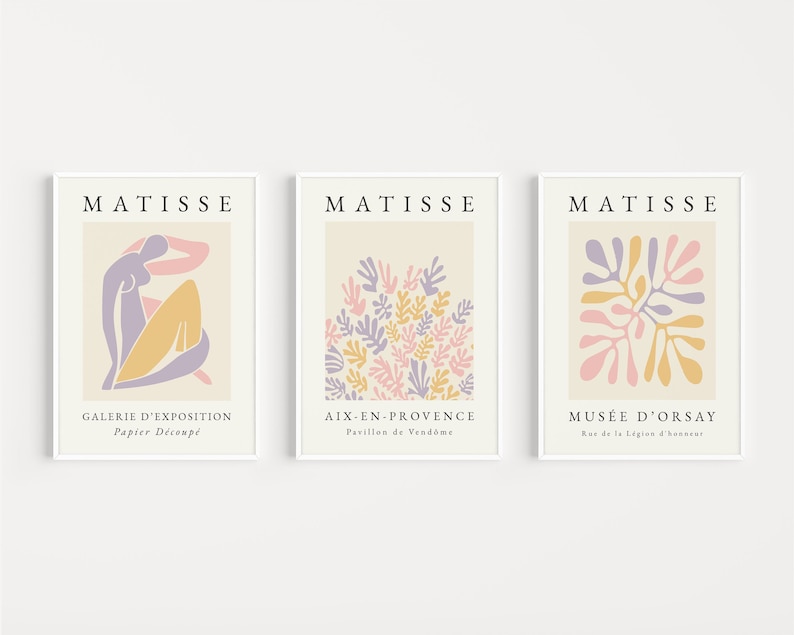 May include: Three minimalist art prints featuring the work of Henri Matisse. The prints are in a white frame and feature a light beige background with a pink, yellow, and purple abstract design. The text "MATISSE" is at the top of each print. The text below the design on each print reads "GALERIE D'EXPOSITION Papier D&eacute;coup&eacute;", "AIX-EN-PROVENCE Pavillon de Vendome", and "MUS&Eacute;E D'ORSAY Rue de la L&eacute;gion d'honneur".