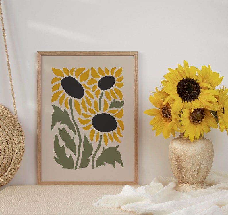 May include: A framed print of a stylized sunflower design in shades of yellow and green. The print is on a cream background and has a wooden frame.