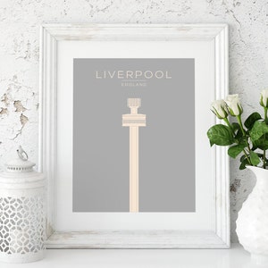 May include: A framed print with a gray background and a white outline. The print features a simple illustration of a tall tower in a light peach color. The text "LIVERPOOL" is at the top of the print in a white font, and the text "ENGLAND" is below it in a smaller white font.