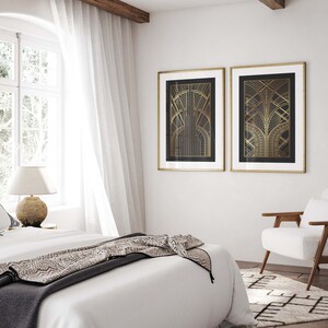 May include: Two gold framed prints with black backgrounds and gold geometric designs hang on a white wall above a white bed with a gray and brown patterned throw blanket.