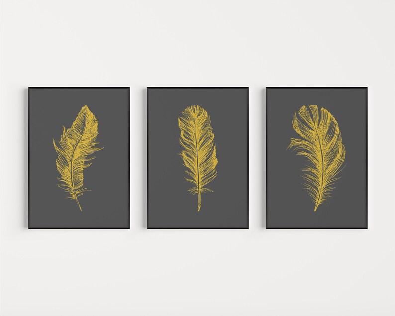 May include: Three framed prints with a dark gray background and a single gold feather illustration on each print.