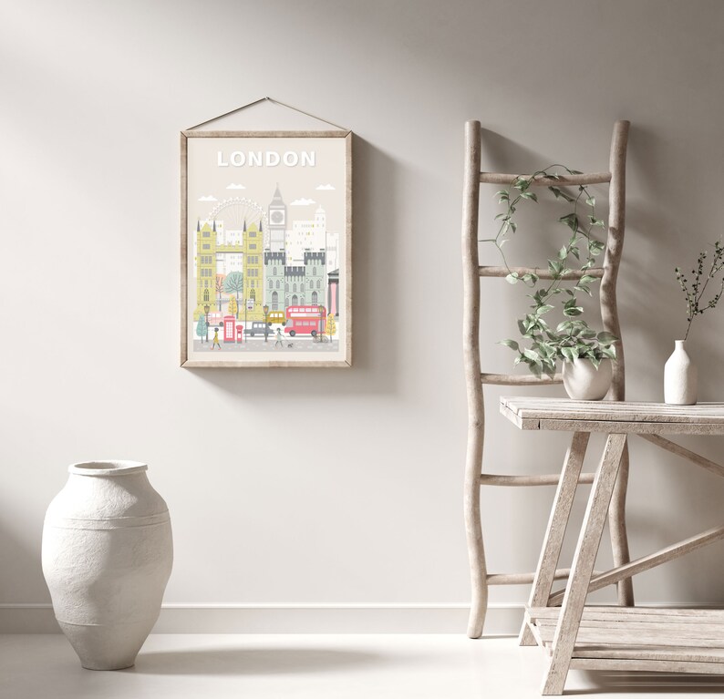Op de afbeelding: Een ingelijste illustratie van de skyline van Londen met het woord "LONDON" in witte tekst bovenaan. De illustratie toont iconische bezienswaardigheden zoals Big Ben, het London Eye en Tower Bridge. De illustratie is in een lichtbeige lijst en hangt aan een witte muur.