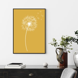 Op de afbeelding: Een minimalistische kunstprint met een witte paardenbloem met zaden die in de wind waaien op een gele achtergrond.
