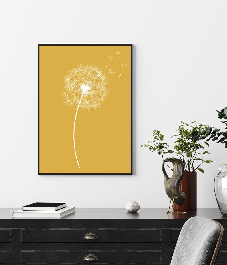 Op de afbeelding: Een minimalistische kunstprint met een witte paardenbloem met zaden die in de wind waaien op een gele achtergrond.
