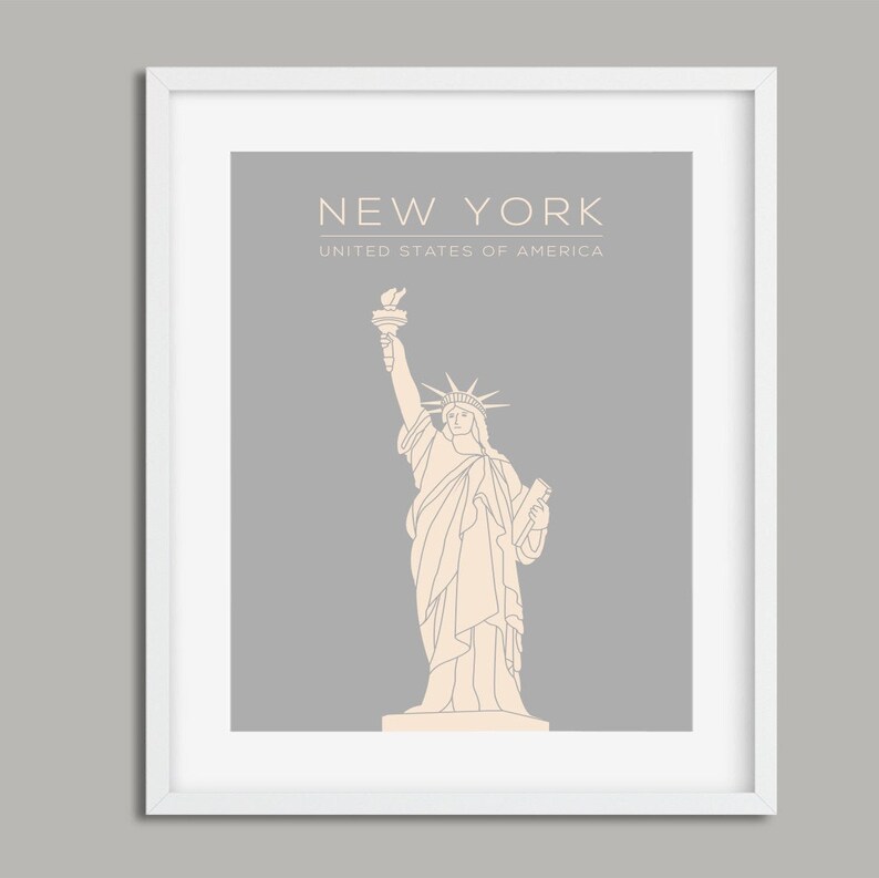 May include: A framed print with a grey background and a white outline. The print features a line drawing of the Statue of Liberty in beige. The text "NEW YORK" and "UNITED STATES OF AMERICA" is printed in white at the top of the print.