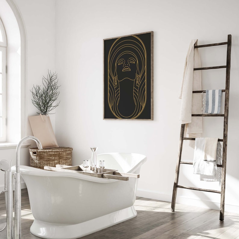 Puede incluir: Una ba&ntilde;era blanca con una bandeja de madera y una impresi&oacute;n enmarcada en dorado de la cara de una mujer sobre un fondo negro. La impresi&oacute;n tiene un contorno dorado y la cara de la mujer mira hacia arriba.