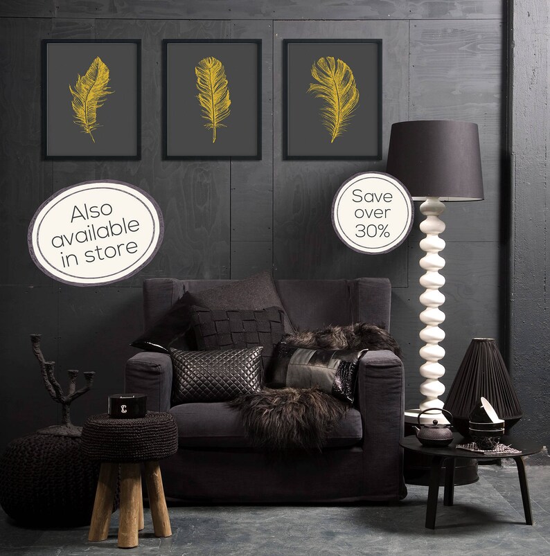 May include: Three framed prints of gold feathers on a dark gray background, hanging on a dark gray wall. A black armchair with black and white pillows sits in front of the prints. A black lamp with a white base stands next to the armchair. A black side table with a black teapot and a black cup sits next to the lamp. The text "Also available in store" and "Save over 30%" is visible in the image.