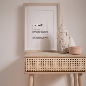 Peut inclure: Une impression encadr&eacute;e avec la d&eacute;finition du mot "&acirc;me s&oelig;ur" en texte noir sur fond blanc. L'impression est pos&eacute;e sur une table en bois clair avec un tiroir en rotin tiss&eacute;. Il y a deux vases en c&eacute;ramique blanche et un r&eacute;cipient en c&eacute;ramique rose sur la table.
